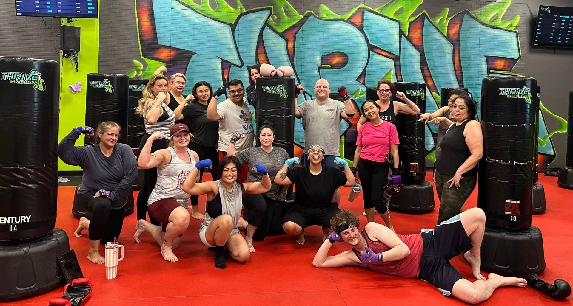 Thrive Kickboxing Henderson members flexing together in front of the gym graffiti wall after a class